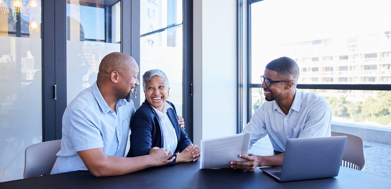 Couple smiling while going over documents with their accountant during a meeting together at table in his office.