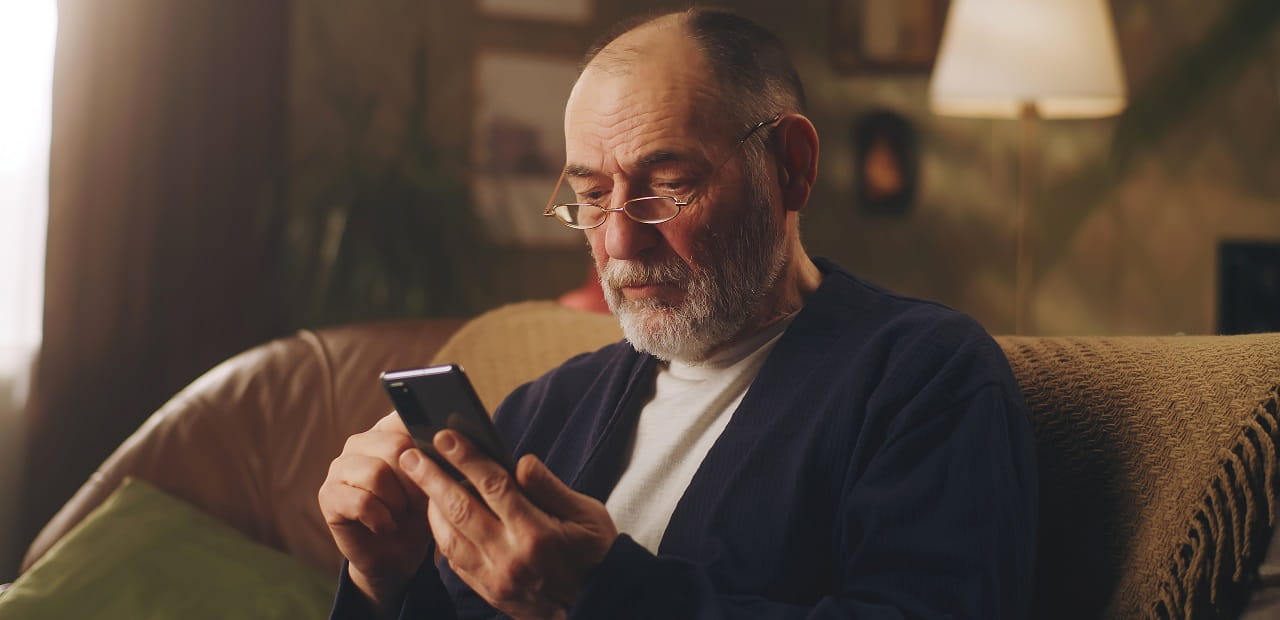 Man with glasses sitting on sofa reading his phone. 