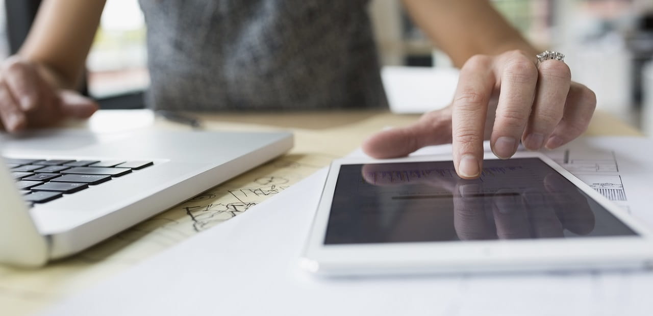 Woman working simultaneously on a laptop and tablet at a desk. 