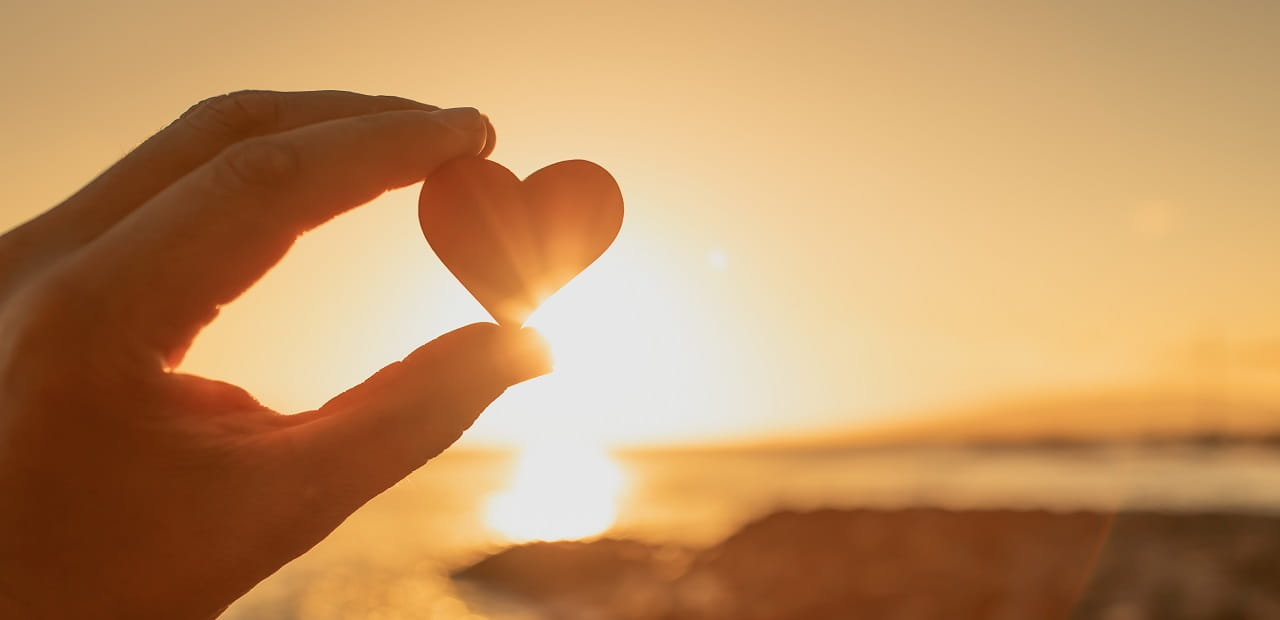 A hand holding heart against a beautiful sunset.