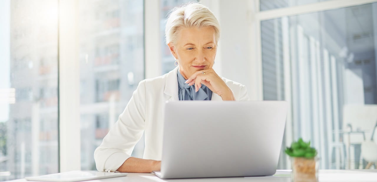 Businesswoman thinking with hand on chin while working on a laptop in an office. 